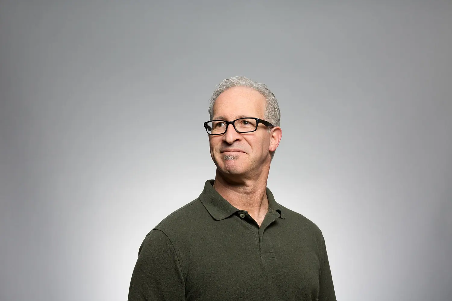 Man with grey hair and glasses against a plain grey studio backdrop.