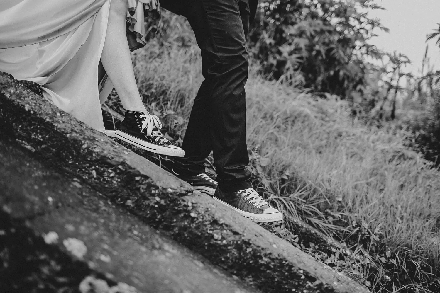 Black and white photo of a wedding couple walking up a grassy slope.