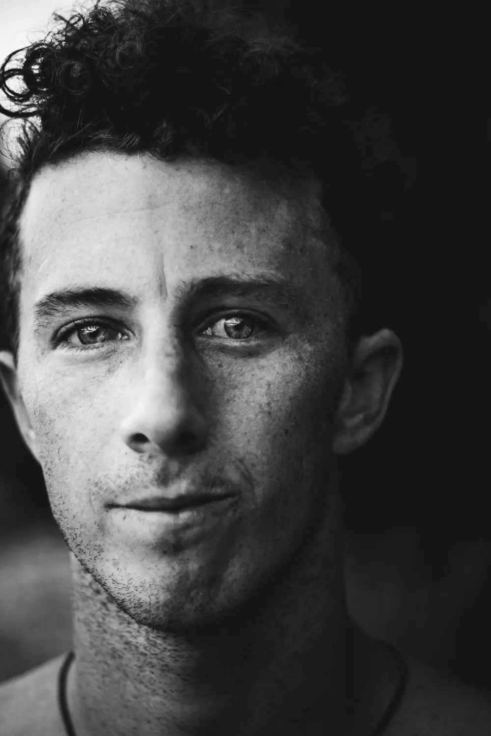 Black and white close portrait of a young man with curly hair and freckles.