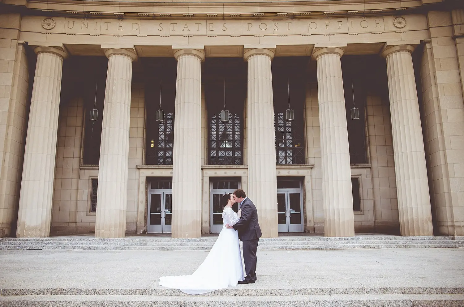 Bride and groom kissing between the columns of an old post office.