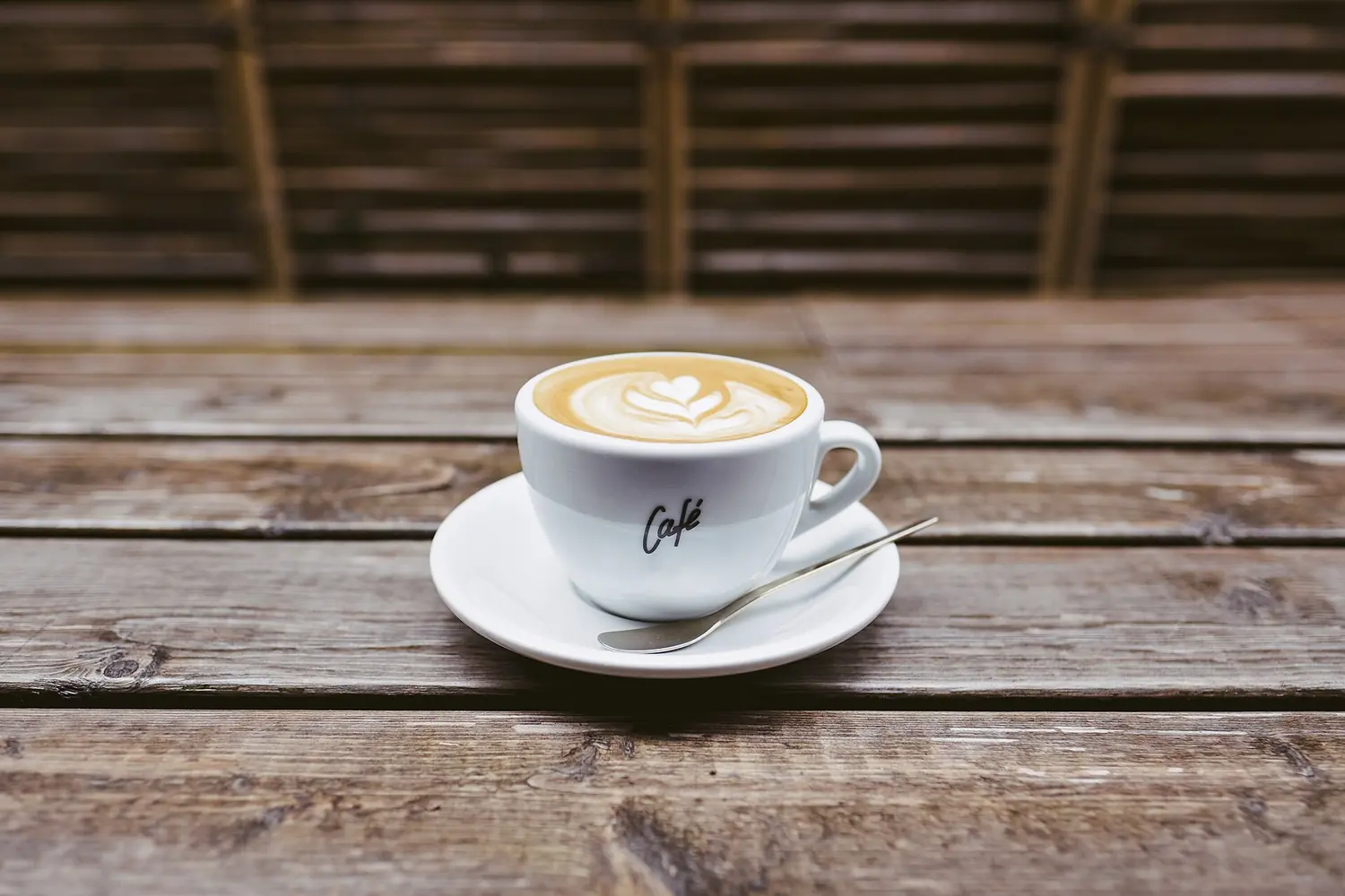 Coffee with latte art in a white cup on a weathered wooden table.