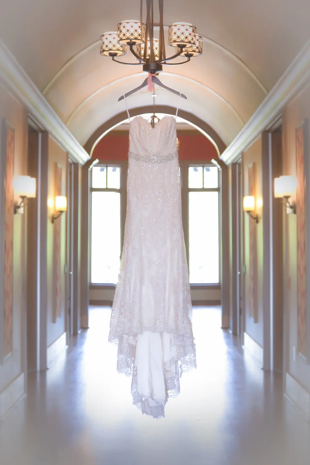 A wedding dress hanging from a chandelier at the end of a hallway.