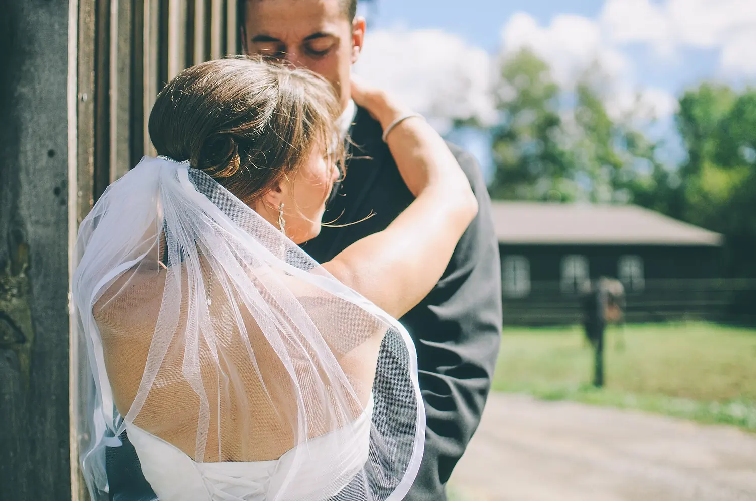 Bride in a veil holding the groom in front of an old wooden building.