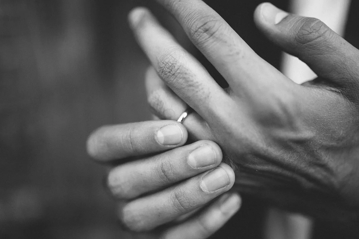 Black and white close-up of two hands and a wedding ring.
